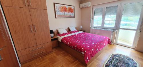 a bedroom with a bed with a red blanket and two windows at Julija 2 in Pančevo
