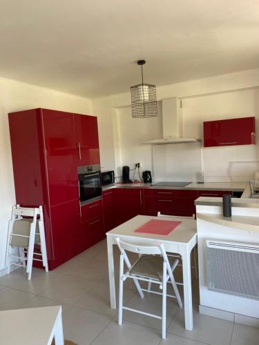 une cuisine avec des placards rouges et une table blanche dans l'établissement Appart 2ème ligne vue mer, 2 chambres, clim, internet, parking, à Palavas-les-Flots