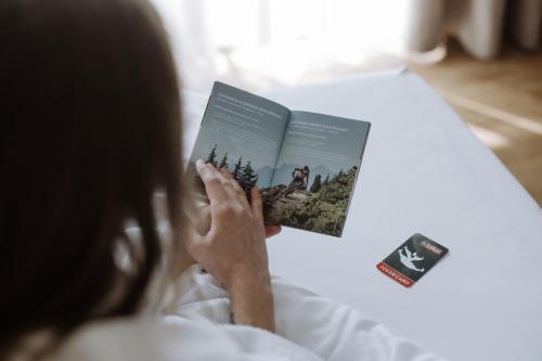 a woman reading a book on a bed at Hotel Sonnegg in Saalbach Hinterglemm