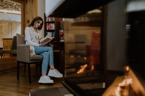 a woman sitting in a chair reading a book at Hotel Sonnegg in Saalbach Hinterglemm