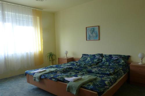 a bedroom with a bed with a blue blanket and a window at Labdarozsa Apartmanhouse in Fonyód
