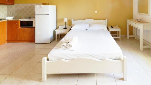 a bedroom with a white bed and a refrigerator at Ενοικιαζόμενα Διαμερίσματα Άρτεμις in Skiros