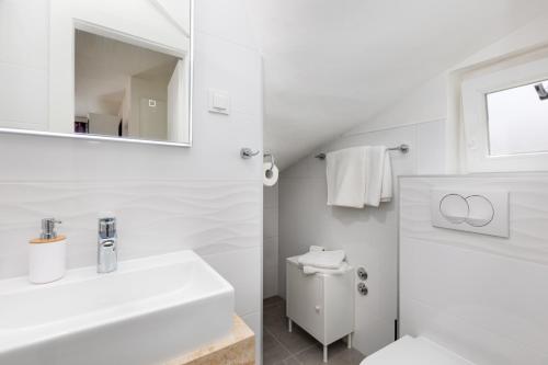a white bathroom with a sink and a mirror at Guest House Šulek in Punat