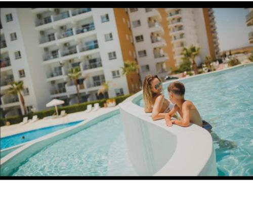 a boy and a girl sitting on a ledge in a swimming pool at Caesar Resort studio in Iskele