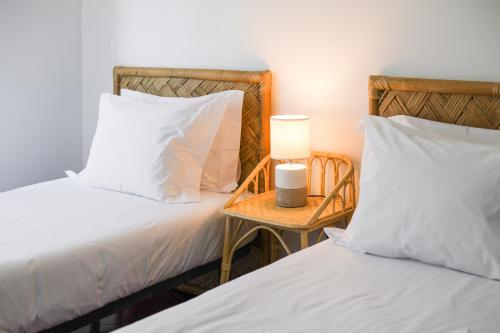 two beds with white pillows and a table with a lamp at Charming TM Flat by the Ocean with a View in Cruz Quebrada