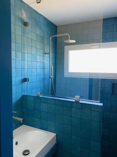 La salle de bains est pourvue de carrelage bleu, d'une douche et d'un lavabo. dans l'établissement Mimosas - Bel appartement avec une vue imprenable sur la baie, à Cavalaire-sur-Mer