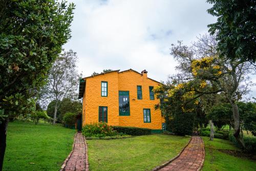 a yellow house on a green field with trees at Estancia San Antonio in Guasca