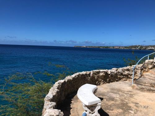 a white bench sitting on a stone wall near the water at Marazul Dive Resort. 3 Bedroom Seafront House. Dive, Snorkel, enjoy amazing sunsets in Westpunt