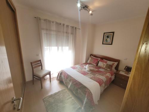 a bedroom with a bed and a chair and a window at Alojamento Valverde in Nazaré