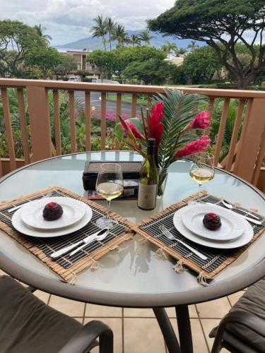 a table with two plates and glasses of wine at Beautiful 2 Bedroom Oceanview Condo at Maui Kamaole Located at South End of Kihei Adjacent to Wailea Traditional Hawaiian Style in Wailea