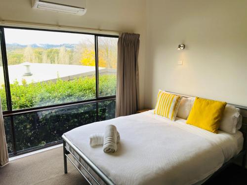 a bedroom with a large bed with yellow pillows and a large window at Cedar Apartments - Merrijig in Merrijig