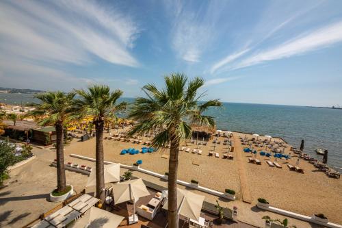 a beach with palm trees and chairs and the ocean at Hotel Zen in Durrës