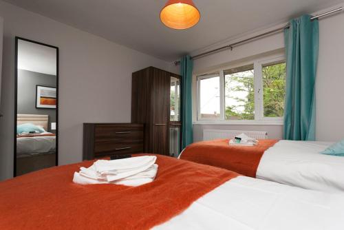 1 Schlafzimmer mit 2 Betten mit orangefarbener Bettwäsche und einem Spiegel in der Unterkunft Comfortable Contractor House Gatwick: sleeps 6+ in Ifield