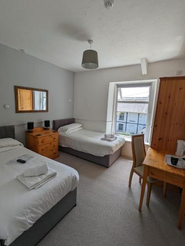 a bedroom with two beds and a desk and a window at Cottage Court Hotel in Tenby