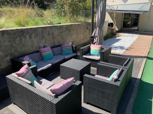 a patio with wicker chairs and a couch with pillows at L'Olivier in Saint-Mitre-les-Remparts