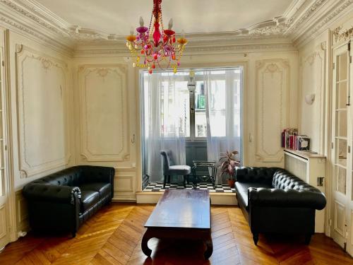 Elle comprend un salon doté d'un mobilier en cuir noir et d'un lustre. dans l'établissement Haussmann Opera Penthouses 130M2, à Paris