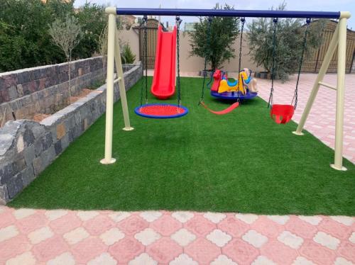 a playground with slides and swings on the grass at Aljabal Al Akhdar Olive Tree Guest house in Al ‘Aqar