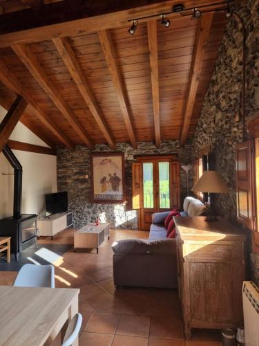 a living room with wooden ceilings and a stone wall at Allotjaments Cal Llarg in Molló