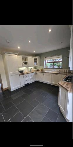 a large kitchen with white cabinets and a tile floor at Sunset cottage in Burry Port