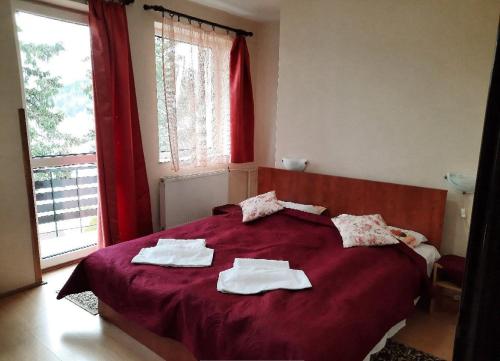 Hotel Priehrada في ديدينكي: غرفة نوم بسرير احمر عليه مناشف