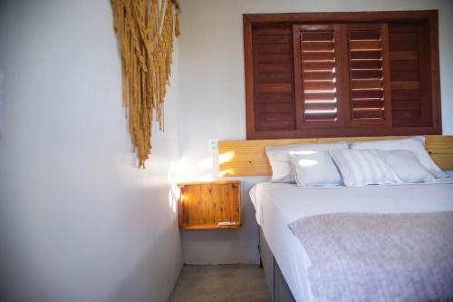 a bedroom with a white bed and a wooden window at Zero Meia Um Pousada in São Miguel do Gostoso