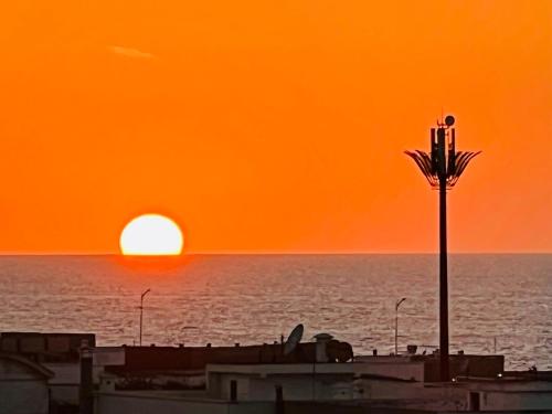 una puesta de sol naranja sobre el océano con una palmera en OceanParc - Vue sur Mer et Parc 24H Sécurité, en Mohammedia
