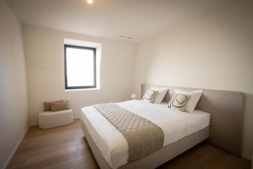 a white bedroom with a large bed with a window at La Risacca, Luxurious, 3 bedroom, sea view design apartment in Cadzand