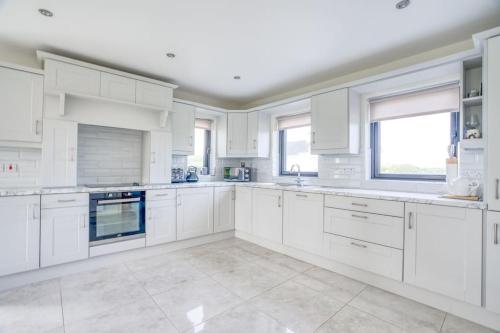 a white kitchen with white cabinets and windows at Teach Trà Murvagh in Mullanacross