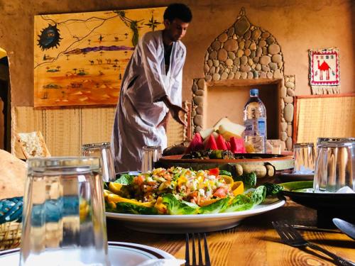 um homem de pé em frente a uma mesa com um prato de comida em Dar Yaya em M'hamid
