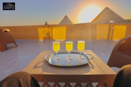 a tray with three wine glasses on a table with pyramids at Tamara Pyramids View in Cairo