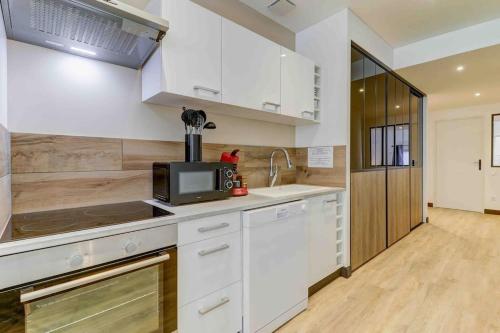 a kitchen with white cabinets and a microwave at LA MANUFACTURE - TOPDESTINATION-BOURG - Centre ville - Classé 3 étoiles in Bourg-en-Bresse