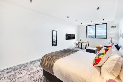 a white bedroom with a large bed and a table at Roomie Apartment Hotel in Auckland