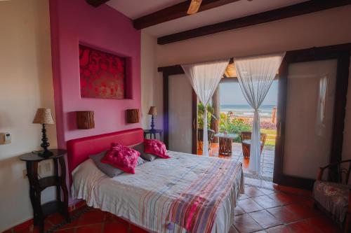a bedroom with a bed with pink walls and a window at Tres Mujeres Hotel in Troncones