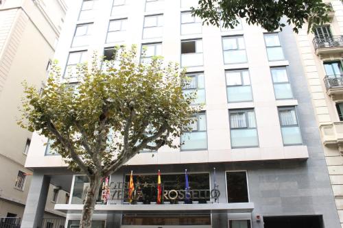 a white building with a tree in front of it at Evenia Rossello in Barcelona