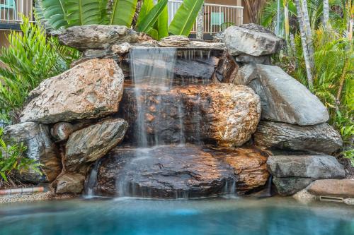 a waterfall in a backyard with rocks and a swimming pool at Hotel Tropiq in Cairns