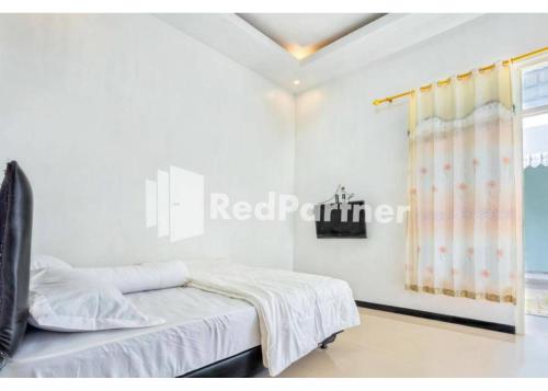 a bedroom with white walls and a bed with a window at Griya Rahayu Guesthouse Mitra RedDoorz near Jatim Park 2 Batu in Tlekung
