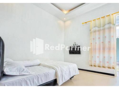 a bedroom with white walls and a bed with a window at Griya Rahayu Guesthouse Mitra RedDoorz near Jatim Park 2 Batu in Tlekung
