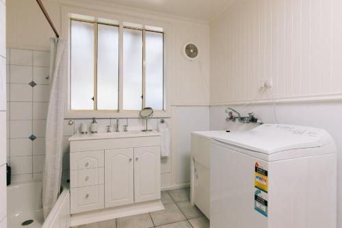 a white bathroom with a sink and a window at Dovestones by the Sea Inverloch in Inverloch