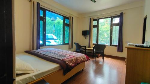 a bedroom with a bed and a desk and windows at The Royal Orchard Kasol in Kasol