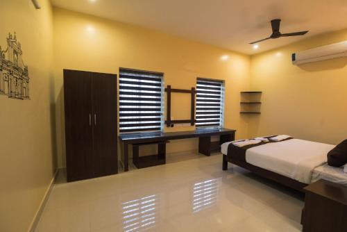 a bedroom with a bed and a desk and windows at Saffron Vilva in Puducherry