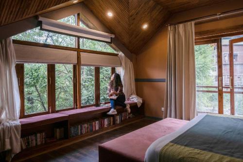 Una bambina seduta sul sedile della finestra in una camera da letto di StayVista at The Artisans' Chalet with Indoor Jacuzzi a Manāli