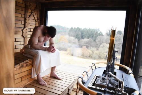 a man sitting on a porch in a room with a window at You and Me Apartments in Prosenická Lhota