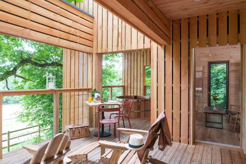 Ce chalet en bois dispose d'une terrasse couverte avec une table et des chaises. dans l'établissement Nuits Perchées, à Maison-Maugis