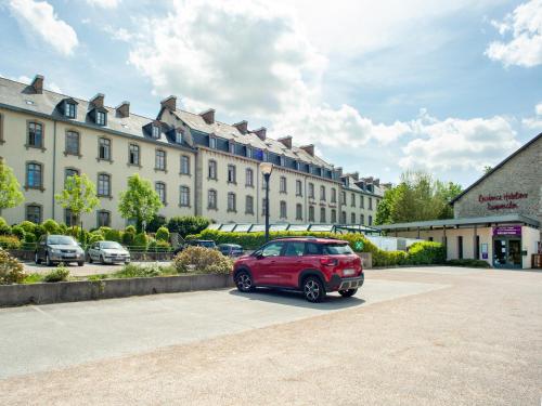 un coche rojo estacionado frente a un gran edificio en Vacancéole - Le Duguesclin, en Dinan