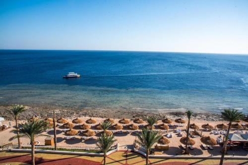a beach with umbrellas and a boat in the water at Sunrise Remal Beach Resort in Sharm El Sheikh
