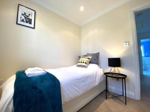 a small bedroom with a white bed and a lamp at NEW! Luxury YELLOW HOUSE Bright Modern Detatched Home with PRIVATE PARKING, NETFLIX Close Luton, M1, and AIRPORT Ideal for Families, Professionals, Consultants, LONGER STAY OPTIONS in Caddington
