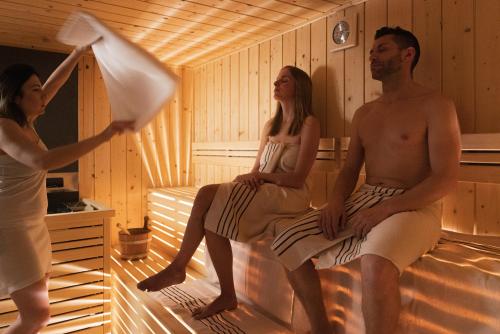 a man and two women sitting in a sauna at Hotel Nele in Ziano di Fiemme
