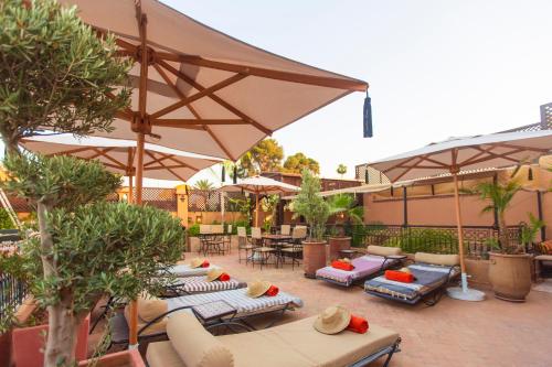 eine Terrasse mit Sonnenschirmen, Liegestühlen und Tischen in der Unterkunft Riad Anya & SPA in Marrakesch