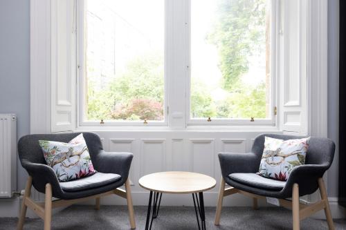 two chairs and a table in a room with two windows at JOIVY Haymarket in Edinburgh