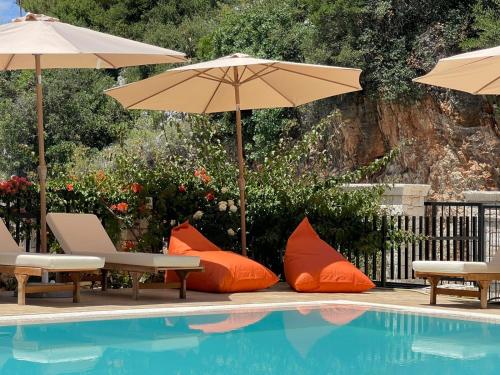 a swimming pool with two umbrellas and orange pillows next to a pool at Hotel Platon in Sarandë